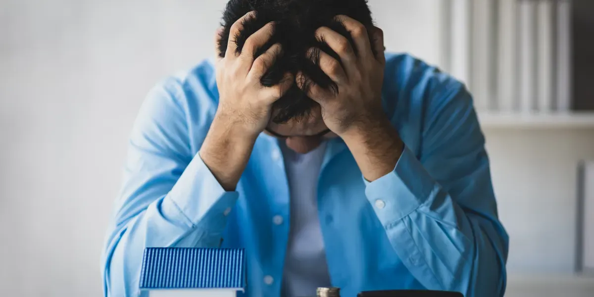Verkäufer sitzt ratlos vor Hausmodell und Münzstapeln